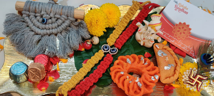 Rakhi Hamper including a woven macrame hanging, colorful rakhi bands, ganpati idol, roli chawal, sweet candles and a rakhi card